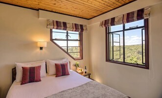 Un dormitorio con cama, dos ventanas, una mesita de noche y una lámpara.
