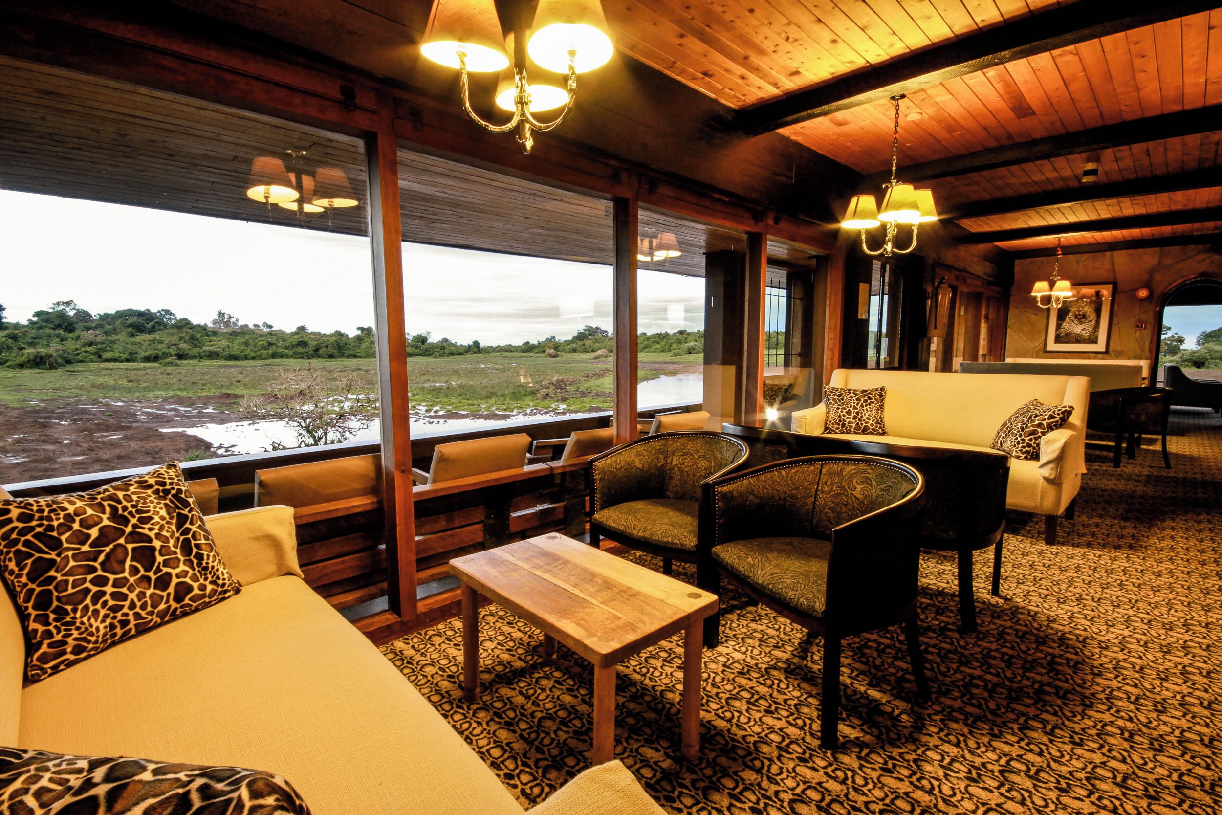 A room with a wooden ceiling, a sofa with giraffe-patterned pillows, a dining table, and chairs.