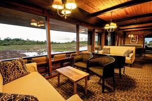 A room with a wooden ceiling, a sofa with giraffe-patterned pillows, a dining table, and chairs.