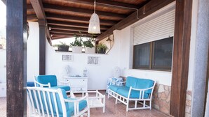A covered patio area with white wicker furniture and blue cushions, potted plants, and a white cabinet.