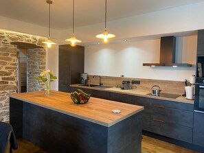 A modern kitchen with a central island, dark cabinetry, a stone accent wall, and pendant lighting. - Propriété à la campagne (Trégunc)