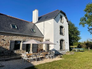 A stone building with a grey roof, a chimney, and a small window. There is a patio with a table and chairs, and a tennis table. - Propriété à la campagne (Trégunc)
