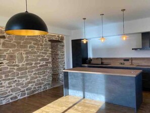 A modern kitchen with a stone accent wall, a central island, and pendant lighting. - Propriété à la campagne (Trégunc)