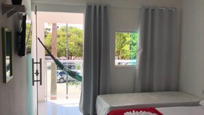 A hotel room with a bed, a red blanket, a window with curtains, and a view of the outside. - Pousada Porto dos Reis (Ipojuca)