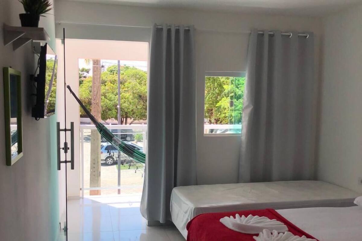 A hotel room with a bed, a red blanket, a window with curtains, and a view of the outside.