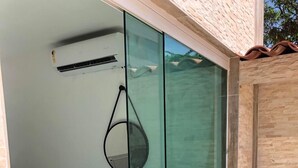 A modern room with a glass door, a blue chair, a small table, and a wall-mounted air conditioner. - Pousada Porto dos Reis (Ipojuca)
