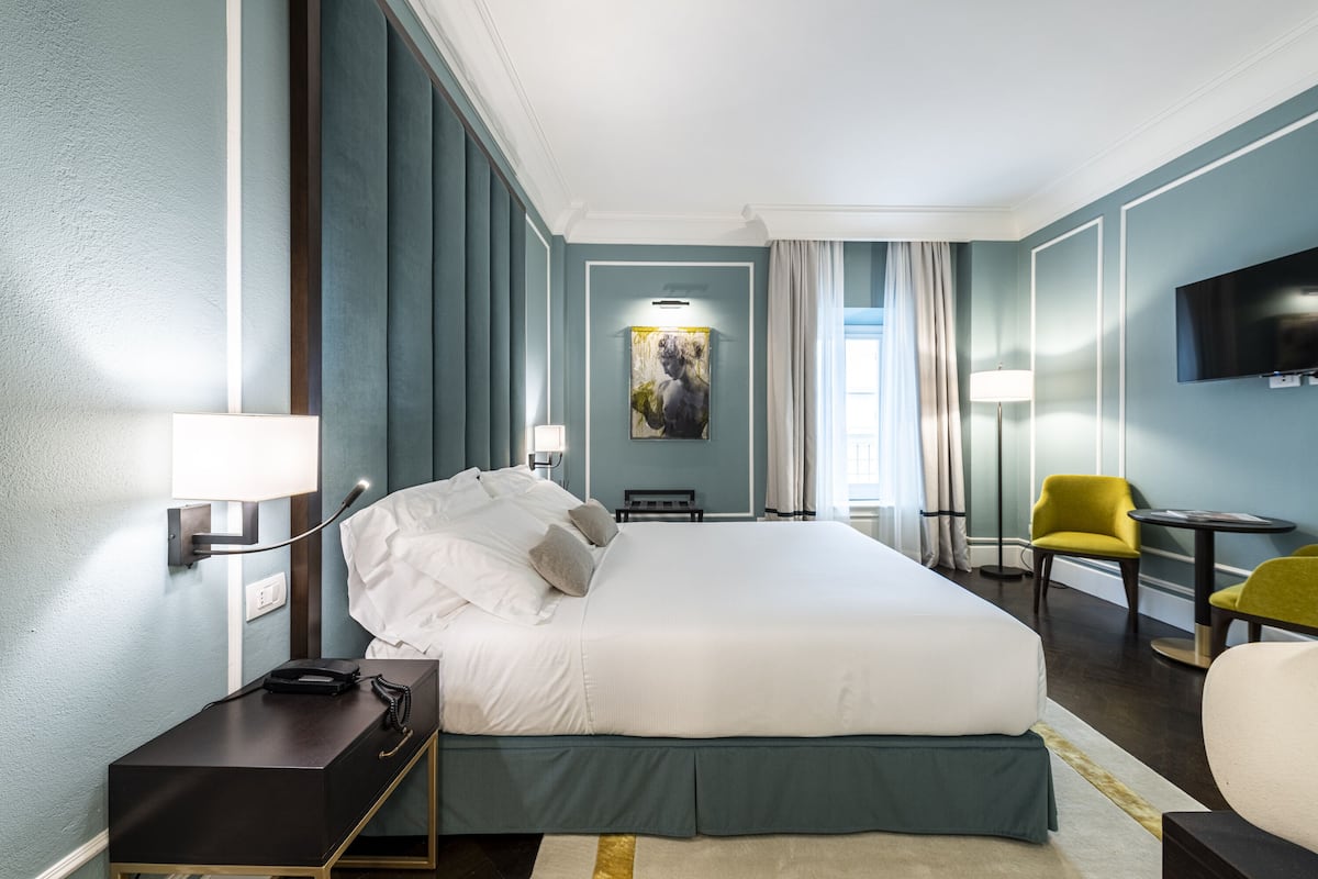 Une chambre d’hôtel avec un grand lit, des tables de chevet, un bureau, une chaise, une télévision et un tableau au mur.