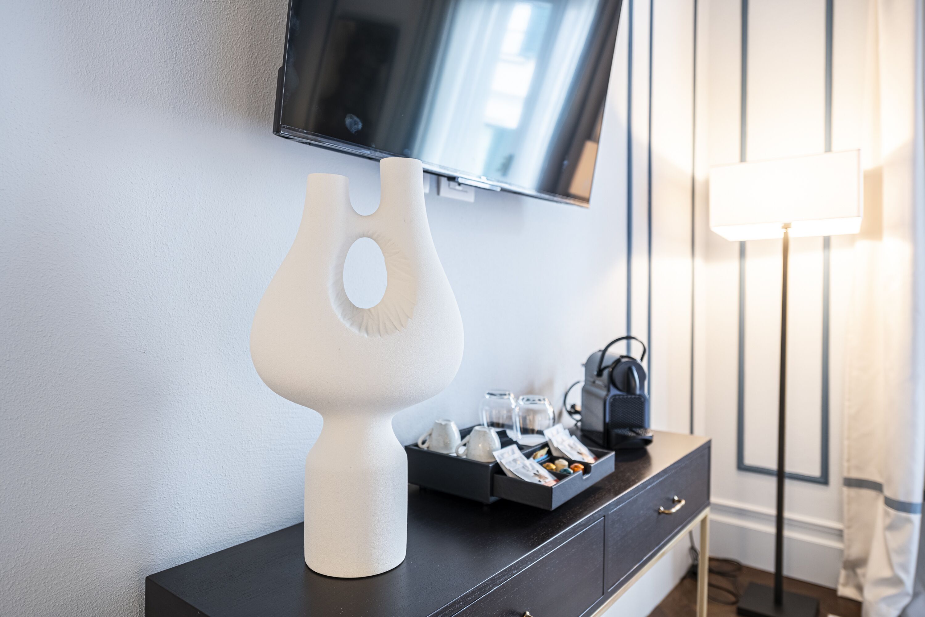 Una habitación moderna con un aparador negro, una escultura abstracta blanca, un televisor de pantalla plana y una lámpara.