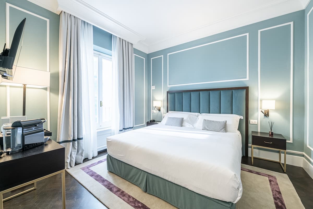 Une chambre d’hôtel bien aménagée, avec un grand lit, des tables de chevet, un bureau avec une imprimante et une fenêtre avec des rideaux.