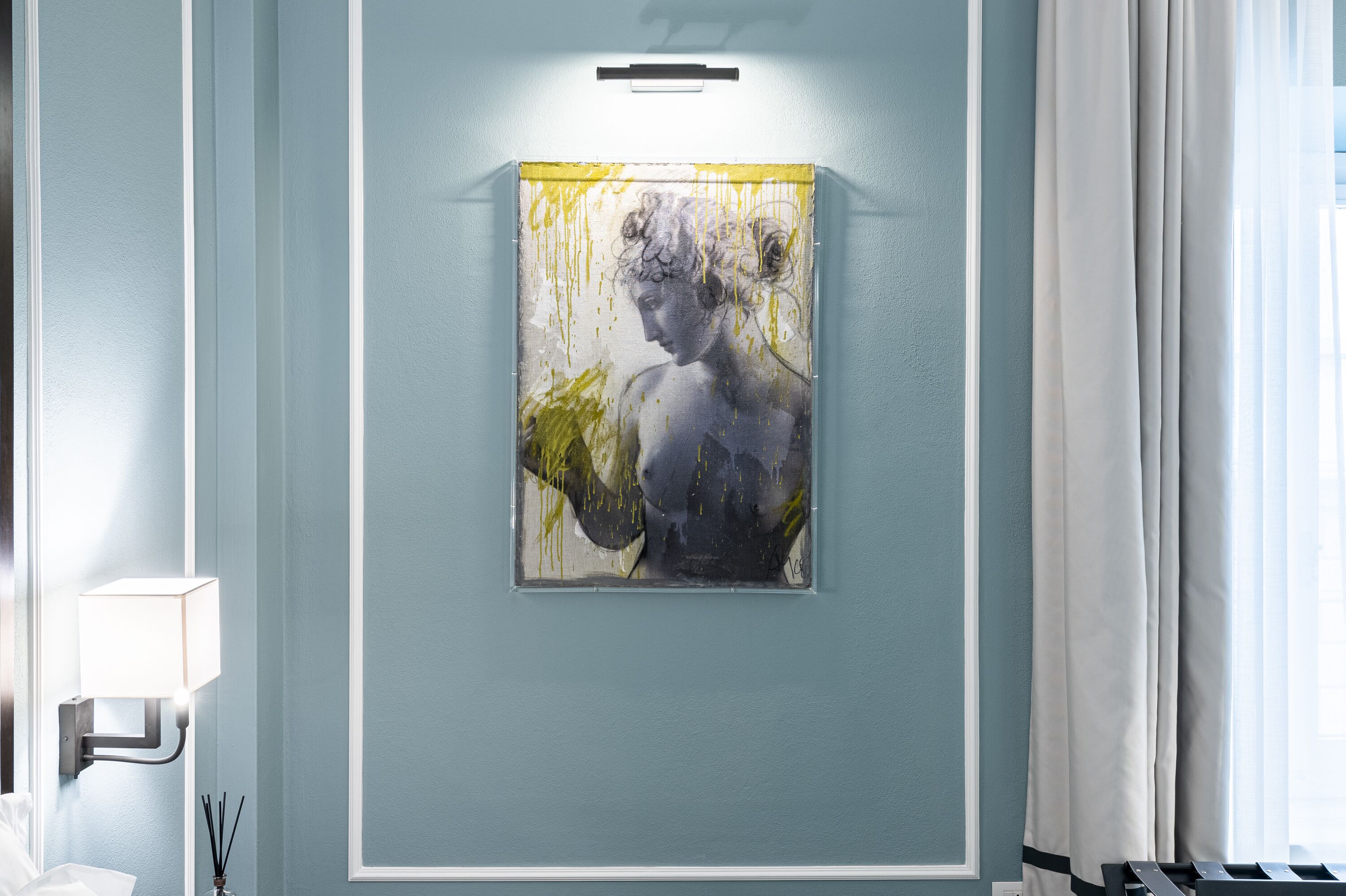 Una obra de arte en un marco en la pared, una lámpara y una ventana con cortinas.