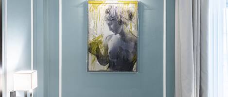 Una obra de arte en un marco en la pared, una lámpara y una ventana con cortinas.