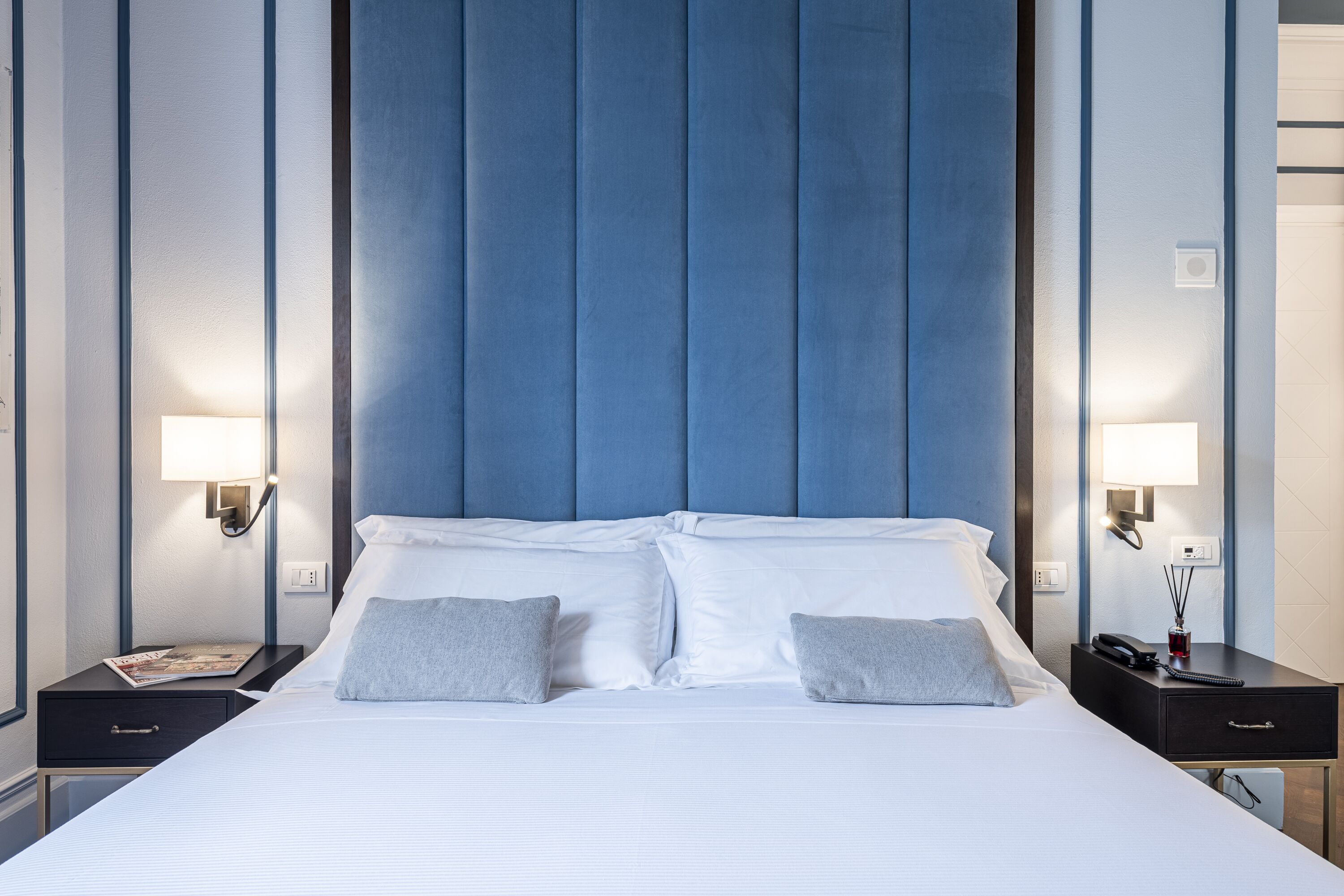 A hotel room with a large bed, two bedside tables, and a blue headboard.