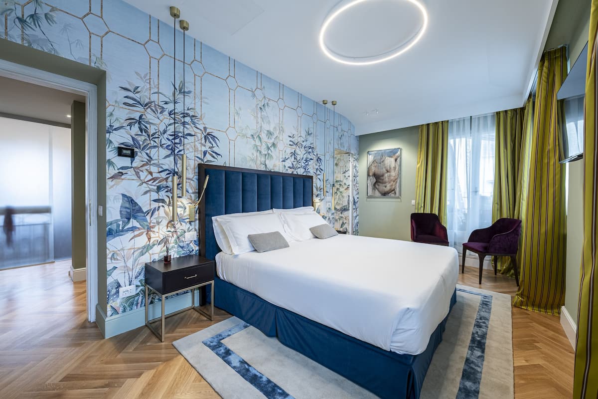 Une chambre moderne avec un grand lit, une table de chevet, une chaise et un mur orné d’un motif floral.