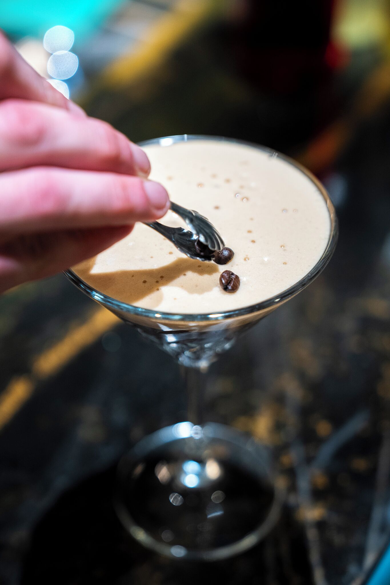A hand holding a fork with a chocolate piece above a frothy beverage in a glass.