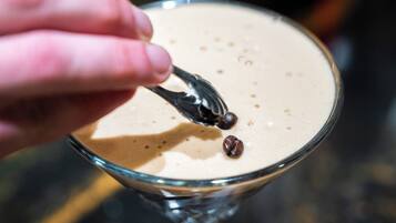 A hand holding a fork with a chocolate piece above a frothy beverage in a glass.