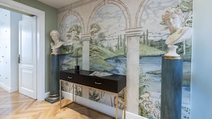 A hallway with a marble mural, a black console table, and classical bust sculptures. - Glimpse Hotel (Florence)