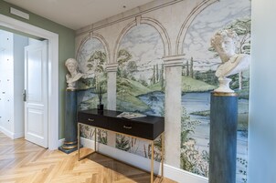 Un corridoio con un affresco in marmo, un tavolo consolle nero e sculture di busti classici.