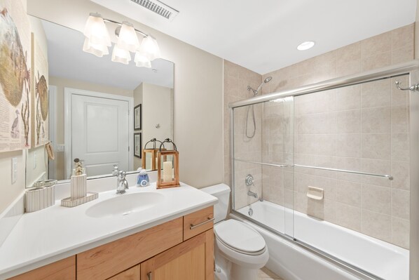 Un baño moderno con un lavabo blanco, tocador de madera, un espejo grande, cabina de ducha con paredes de vidrio y un inodoro.
