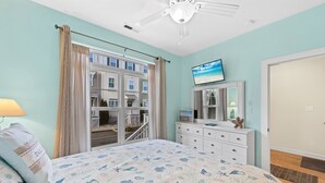 A bedroom with a bed, a dresser, a television, and a window with curtains.