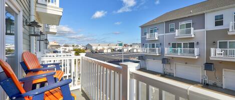 A balcony with two Adirondack chairs, a white railing, and a view of a street with buildings.