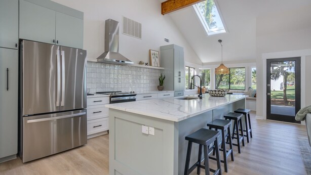 A modern kitchen with a large island, stainless steel appliances, and a skylight.