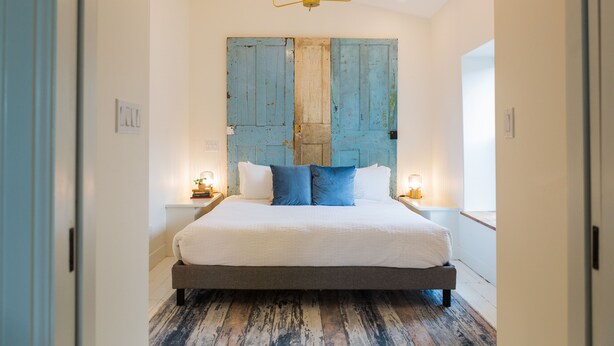 A bedroom with a large bed, wooden headboard, bedside lamps, and a chandelier. - Stylish, spacious suite in Wellington- steps to beach, dining, brewery and shops (Prince Edward)