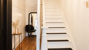 A staircase with white steps and black risers, a black chair, and a vase with dried flowers on a small table. - Stylish, spacious suite in Wellington- steps to beach, dining, brewery and shops (Prince Edward)