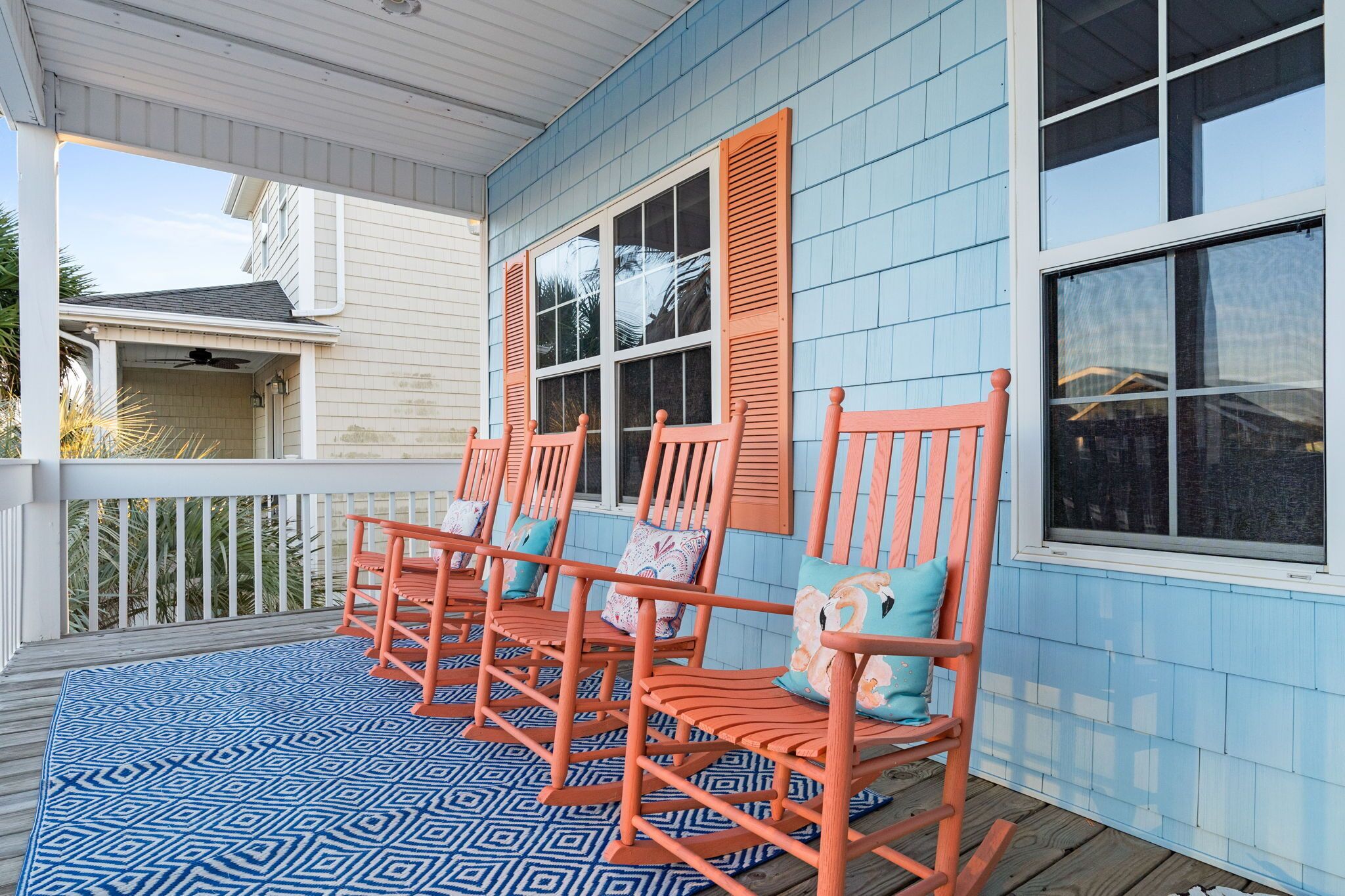 A porch with three rocking chairs and a blue patterned rug.