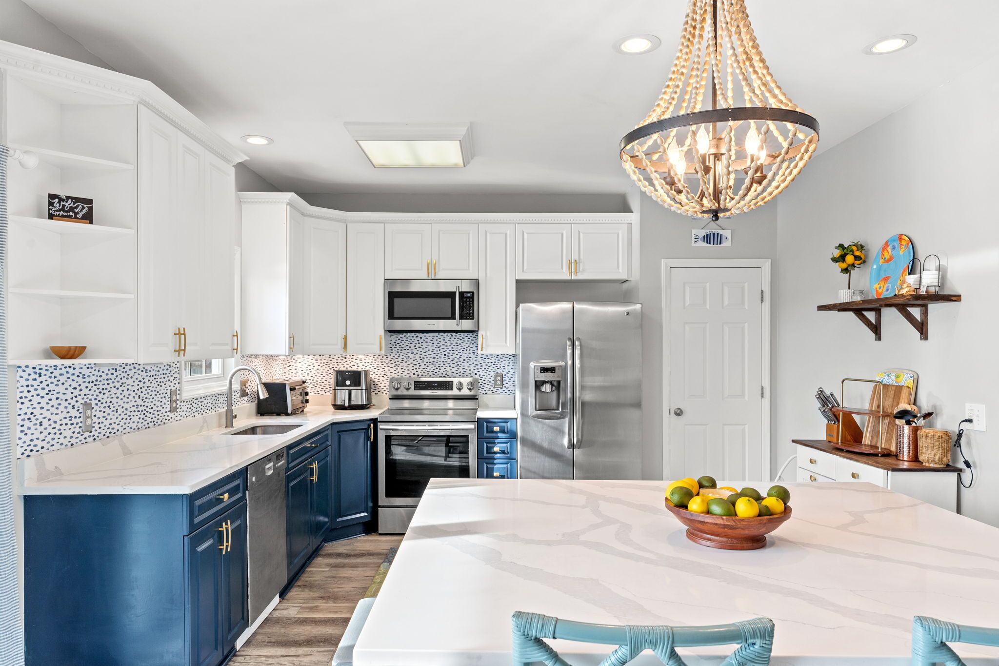 A modern kitchen with white cabinets, a blue island, stainless steel appliances, and a chandelier.
