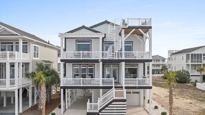 A multi-story beachfront house with balconies, a staircase, and a sandy driveway. - Oyster Perpetual, 5 bedroom 5 bathroom home that ensures your stay is timeless. (Ocean Isle Beach)