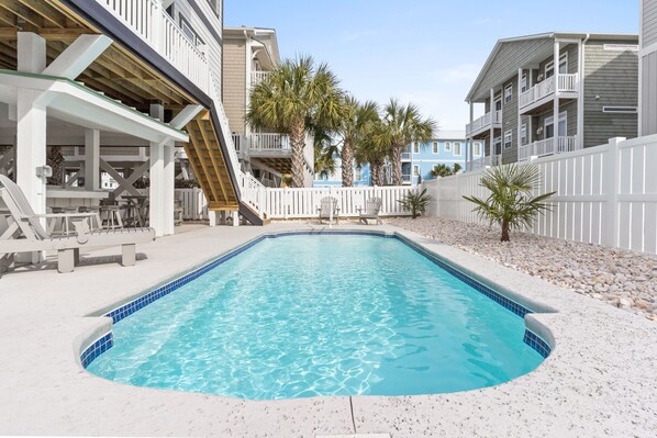 A swimming pool with a white deck, surrounded by a white fence and palm trees.