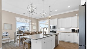 A modern kitchen with white cabinets, a large island, and pendant lighting. - Oyster Perpetual, 5 bedroom 5 bathroom home that ensures your stay is timeless. (Ocean Isle Beach)