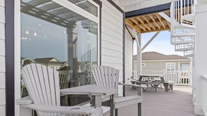 A covered outdoor deck with Adirondack chairs and picnic tables. - Oyster Perpetual, 5 bedroom 5 bathroom home that ensures your stay is timeless. (Ocean Isle Beach)