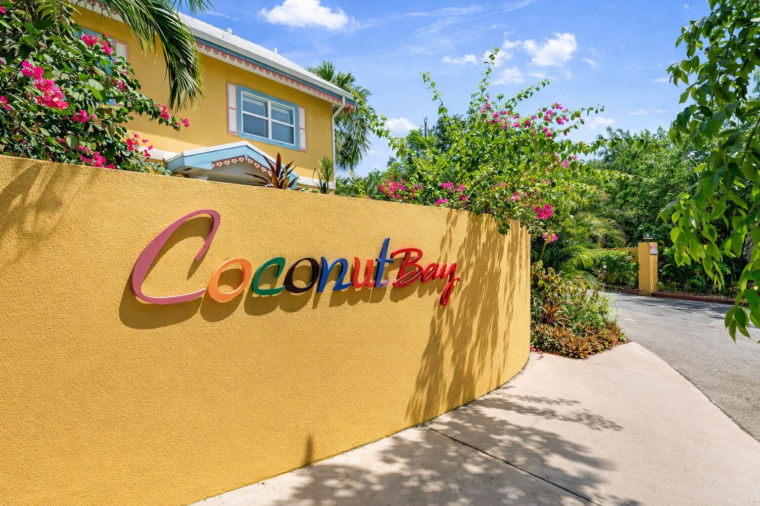 Une enseigne avec l’inscription « Coconut Bay » en lettres colorées sur un mur jaune.