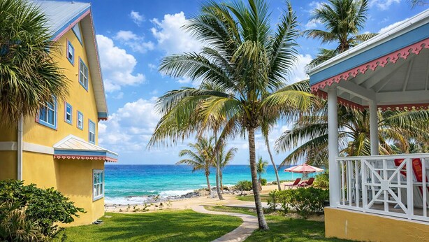 A beachfront property with a pathway leading to a covered area with chairs and umbrellas, overlooking the ocean.
