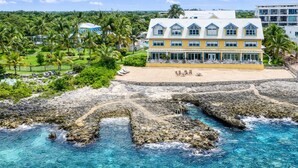 A coastal hotel with a beach, clear waters, and a rocky shoreline.