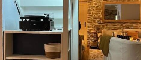 A room with a wooden floor, a white wall with a built-in shelf holding baskets, and a stone wall with a fireplace.