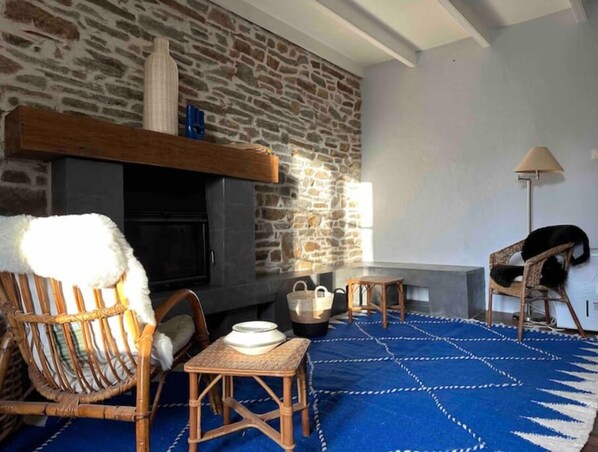 Uma sala de estar acolhedora com parede de pedra, lareira, móveis de vime e um tapete azul estampado.