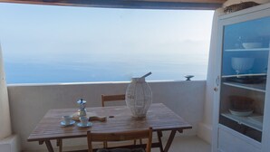 A wooden table with a white vase and cups on a balcony overlooking the sea.