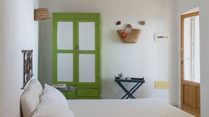 A bedroom with a bed, a green wardrobe, a small table with a cup and a bowl, and a window with a view.