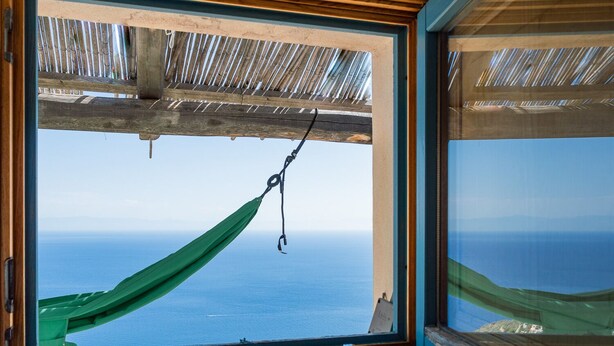 A hammock hanging by a window overlooking a clear blue sea.