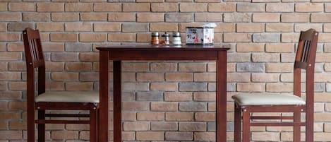 Dos sillas de madera con asientos y respaldos acolchados, una pequeña mesa de madera con algunos objetos encima, y un muro de ladrillo al fondo.