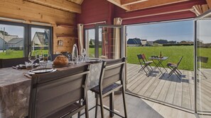 A wooden interior with a dining area, a table set for two, and a view of a grassy outdoor deck. - 650 m from the beach, chalet with terrace for 4 (Penmarch)