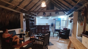 A rustic interior with a thatched roof, wooden furniture, and a person sitting on a couch. - Hostal Principio Tayrona (Santa Marta)