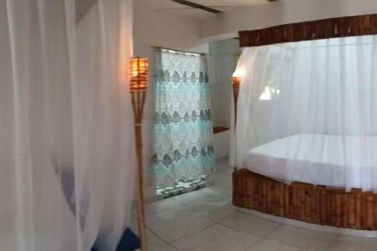 A hotel room with a bed, a wooden headboard, and a window with sheer curtains.