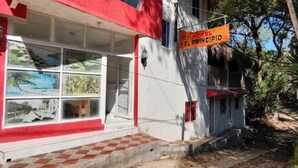 A building with a sign reading "HOTEL EL PRINCIPIO." It has a red awning, a checkered tile entrance, and a window with a view of palm trees. - Hostal Principio Tayrona (Santa Marta)