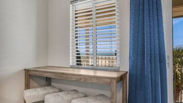 A room with a wooden table, two grey cushioned stools, a window with blinds, and a blue curtain.