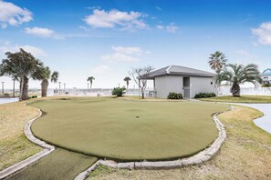 Un campo da golf con un green curato, un edificio a tetto piatto e palme.