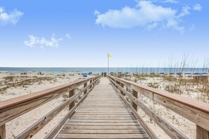 Una passerella di legno che conduce a una spiaggia con ombrelloni e persone.