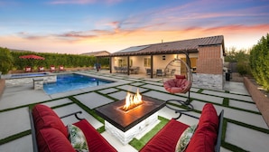 Un patio moderno al aire libre con piscina, una fogata y mobiliario exterior.